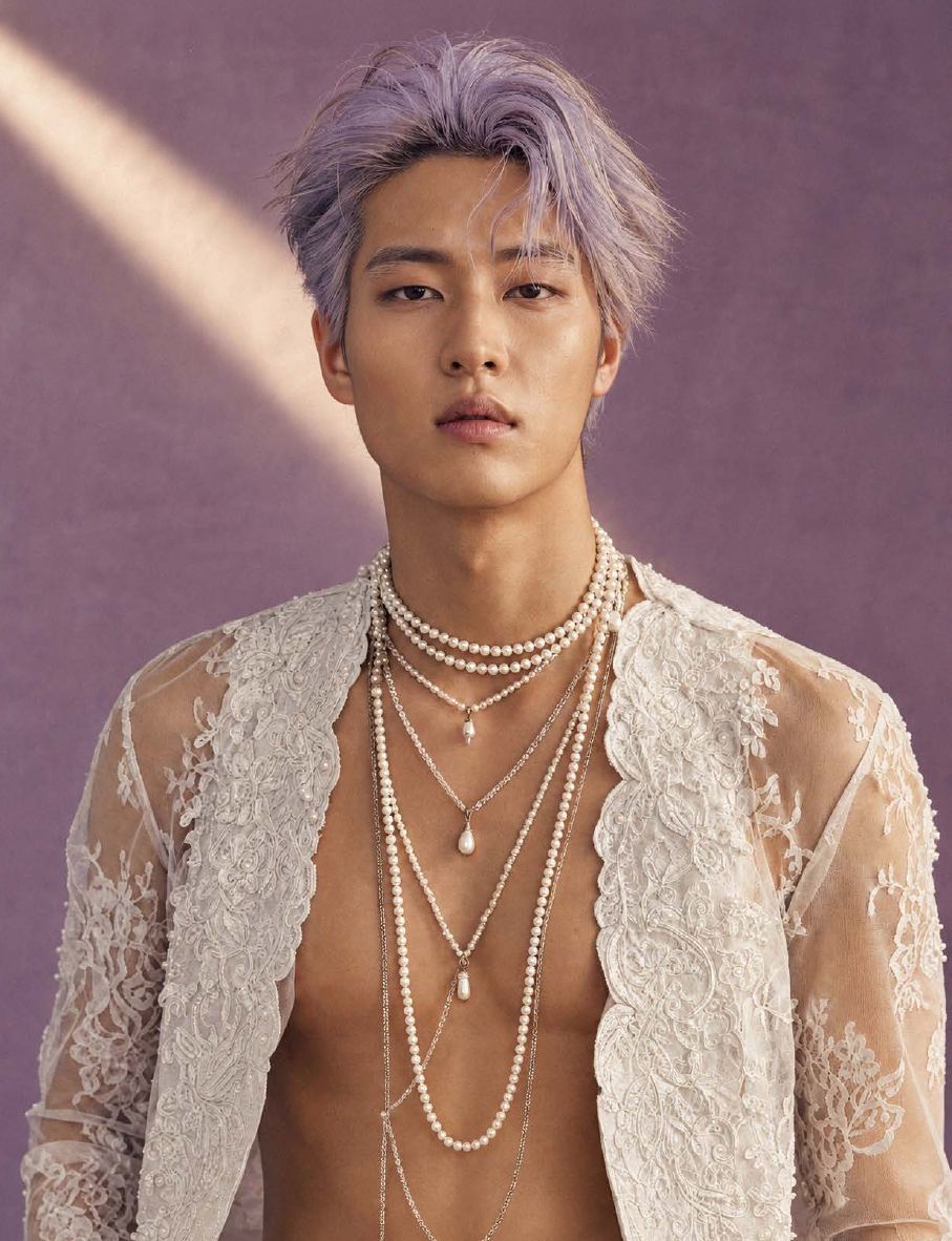 A man with lavender hair wearing layered pearls and an open lace jacket
